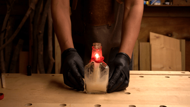 Person holding a lit candle in a bottle