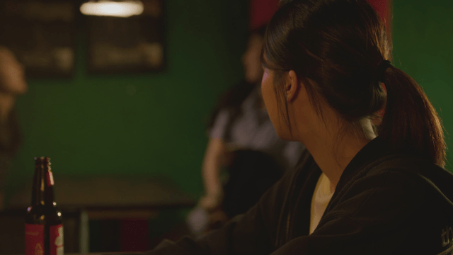 Lonely woman sitting in a dark bar with a beer bottle