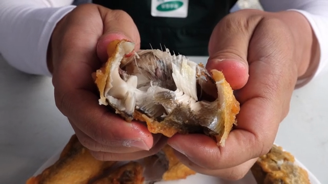 Hands breaking open a fried fish