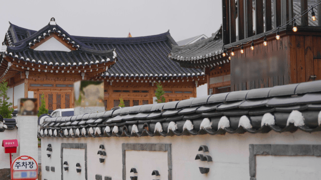 Traditional hanok roof beyond a wall on a rainy day