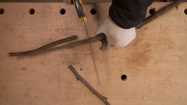 Saw cutting branches on wooden workbench