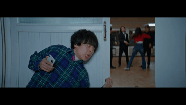 Man calling the police on his phone beyond a door where people are fighting