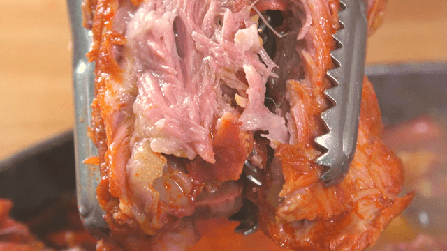 Tongs holding juicy pork back-bone meat from outer leaves stew