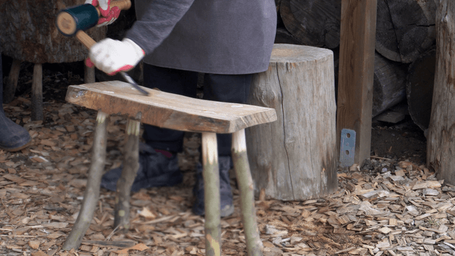 Person crafting a wooden stool outdoors