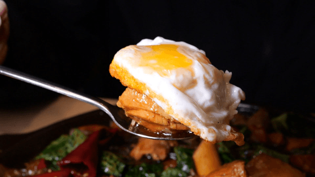 Spoon holding fried egg and braised chicken