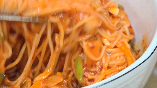Spicy noodles being mixed in a bowl