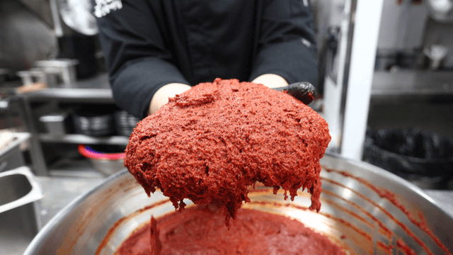 Cook holding mixed chili seasoning in large metal bowl