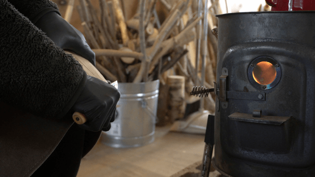 Carpenter carving wood beside a warm stove