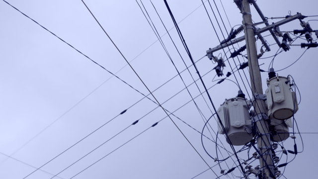 Electric pole with wires against cloudy sky