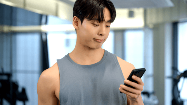 Man using smartphone while lifting a small dumbbell at gym