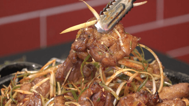 Tongs lifting grilled pork belly with green onions