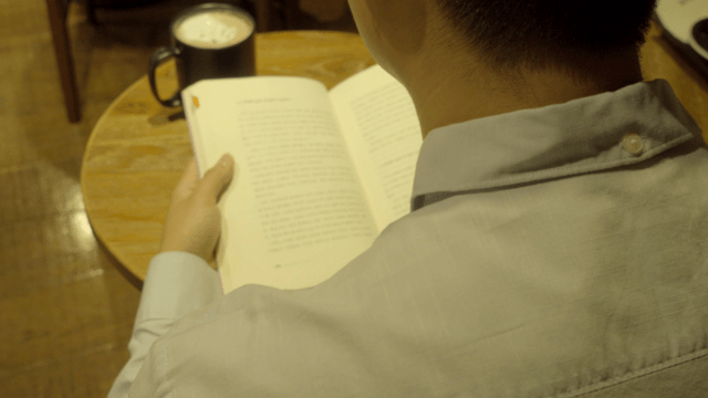 Person reading a book with a coffee nearby