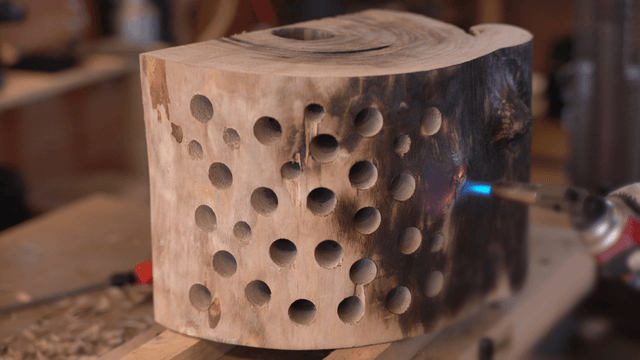 Artisan burning a perforated wooden sculpture with a torch