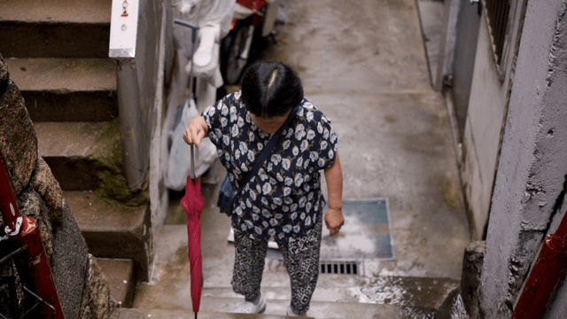 An elderly woman climbing stairs with an umbrella