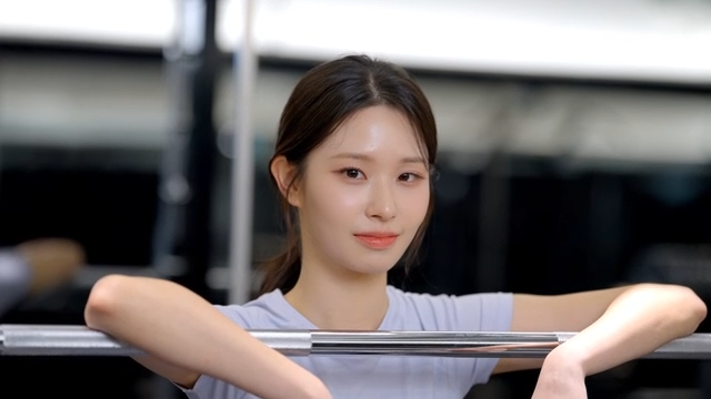 Young woman smiling while resting on a barbell at the gym