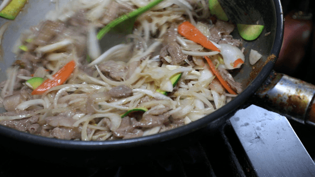 Bulgogi being stir-fried with vegetables in a pan