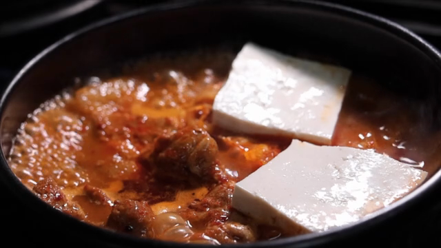 Tofu being placed on top of simmering braised kimchi