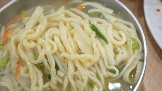 Chopsticks stirring steaming hand-cut noodles
