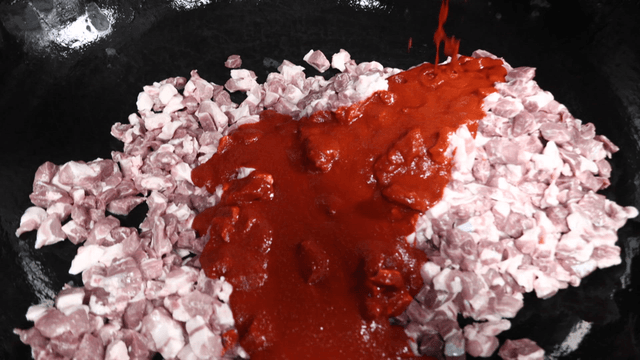 Spicy sauce poured over meat pieces in large pot