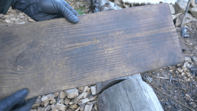 Worker inspecting burned wooden boards in outdoor workshop
