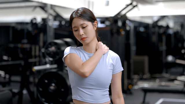 Young woman massaging her shoulder in a gym