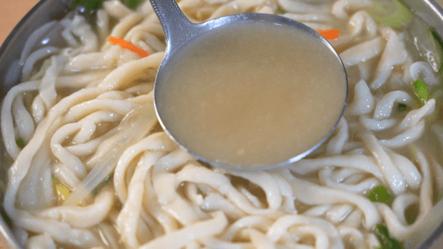 Hand-cut noodles scooped with a ladle in rich broth