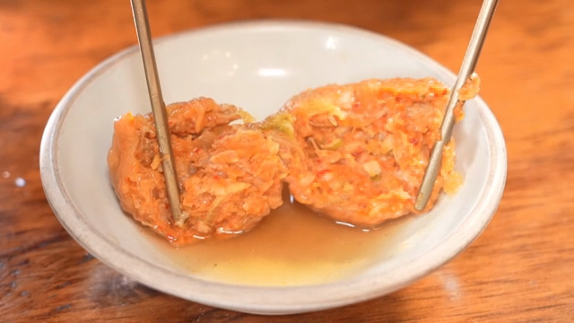 Kimchi dumpling being split with chopsticks