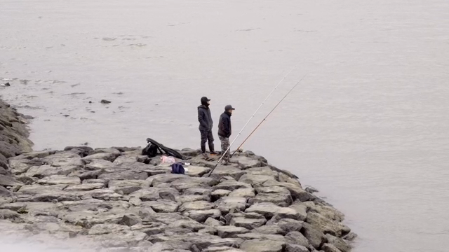 Two people fishing on a rocky shore