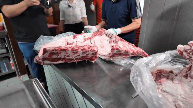 Butchers processing Korean beef cuts with a cameraman filming