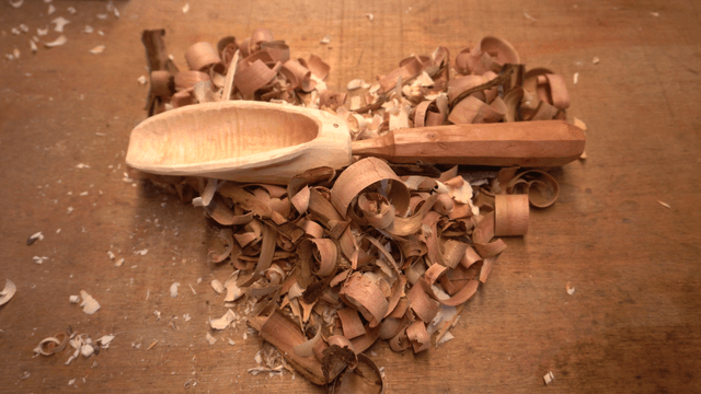 Unique wooden spoon surrounded by sawdust on workbench