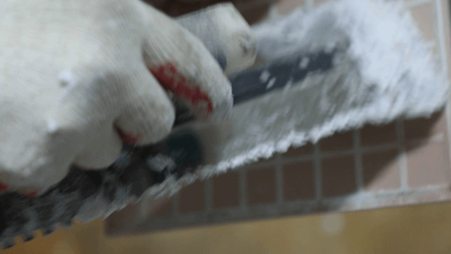 Worker applying adhesive on a tile surface
