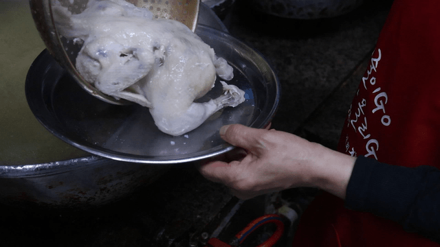 Chef scooping boiled chicken with a strainer
