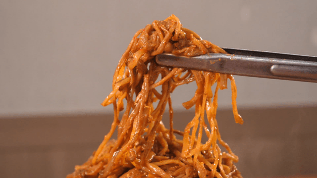 Sweet potato stems from pork backbone stew being lifted with tongs