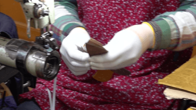 Worker assembling leather pieces with sewing machine