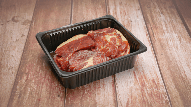 Fresh raw marinated pork in a black plastic tray