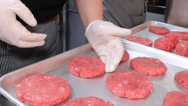 Gloved hands shaping raw meat patties