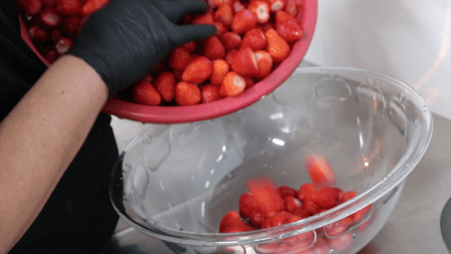 Strawberries being transferred into a transparent bowl