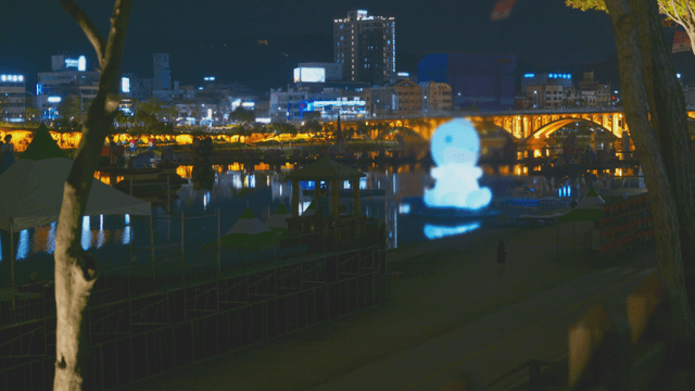 Night scene with bridge and city lights above floating sculpture