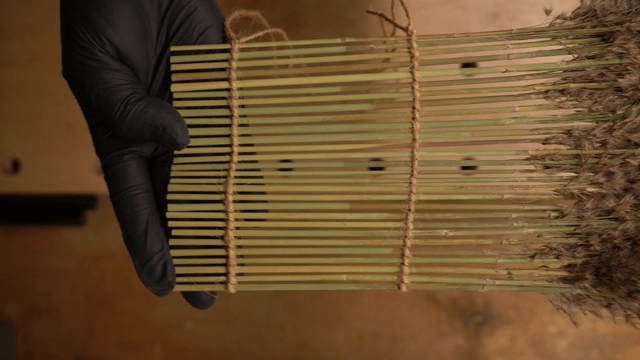 Hands crafting with reeds on a table