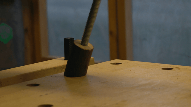 Hand inspecting a wooden block connected to a metal rod