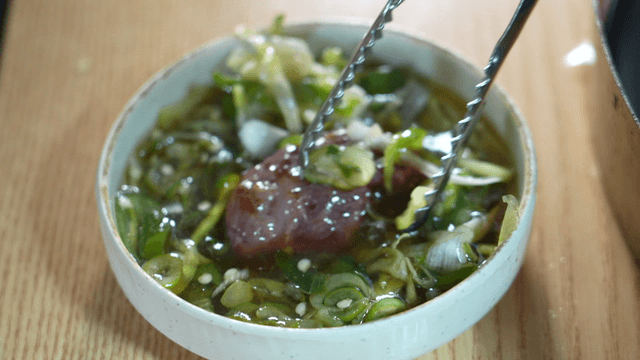 Tongs dipping grilled beef into scallion seasoning sauce
