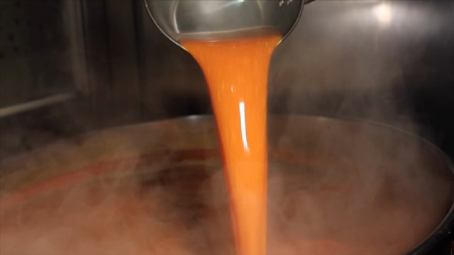 Ladle pouring red broth into a pot