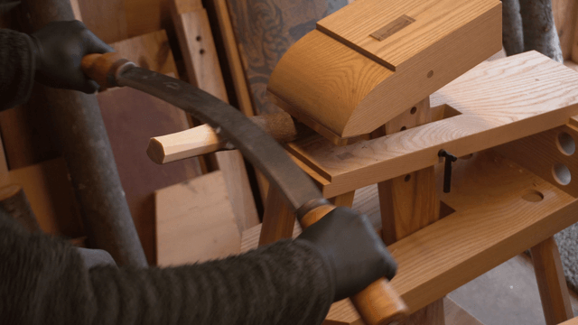 Craftsman shaving a wooden stick with drawknife in workshop