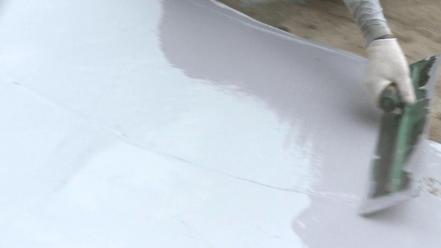 Worker applying white paint coating on cement floor