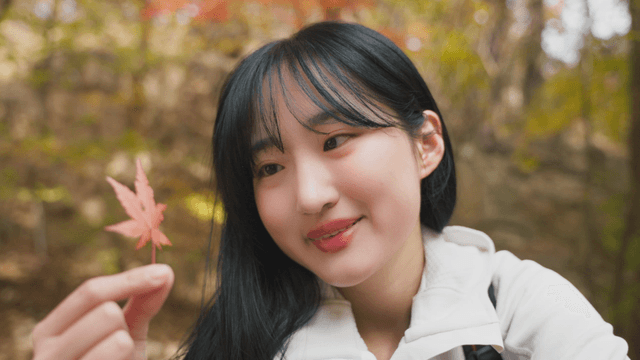 Young woman smiling while holding red autumn maple leaf