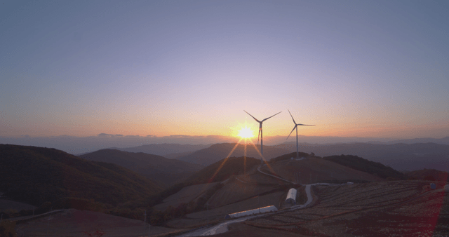 언덕 밭 위의 풍력 터빈 옆 빛나는 일출