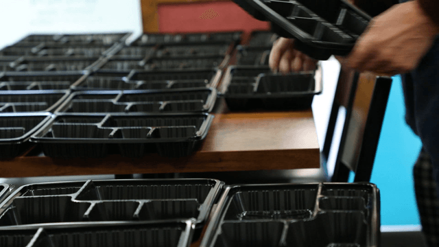 Hands arranging black food trays on a table