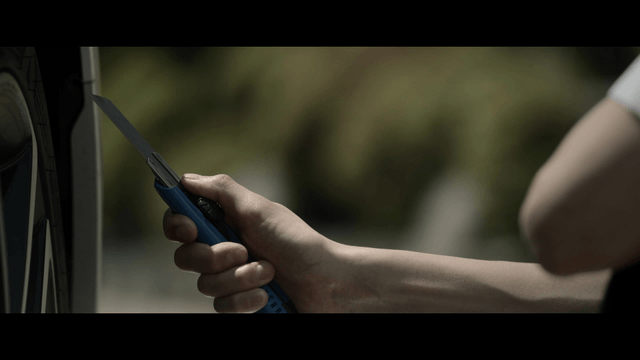 Student holding utility knife beside car tire