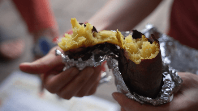 Hands splitting roasted sweet potato in half