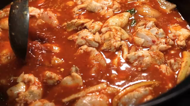 Spicy braised chicken being stirred with a ladle